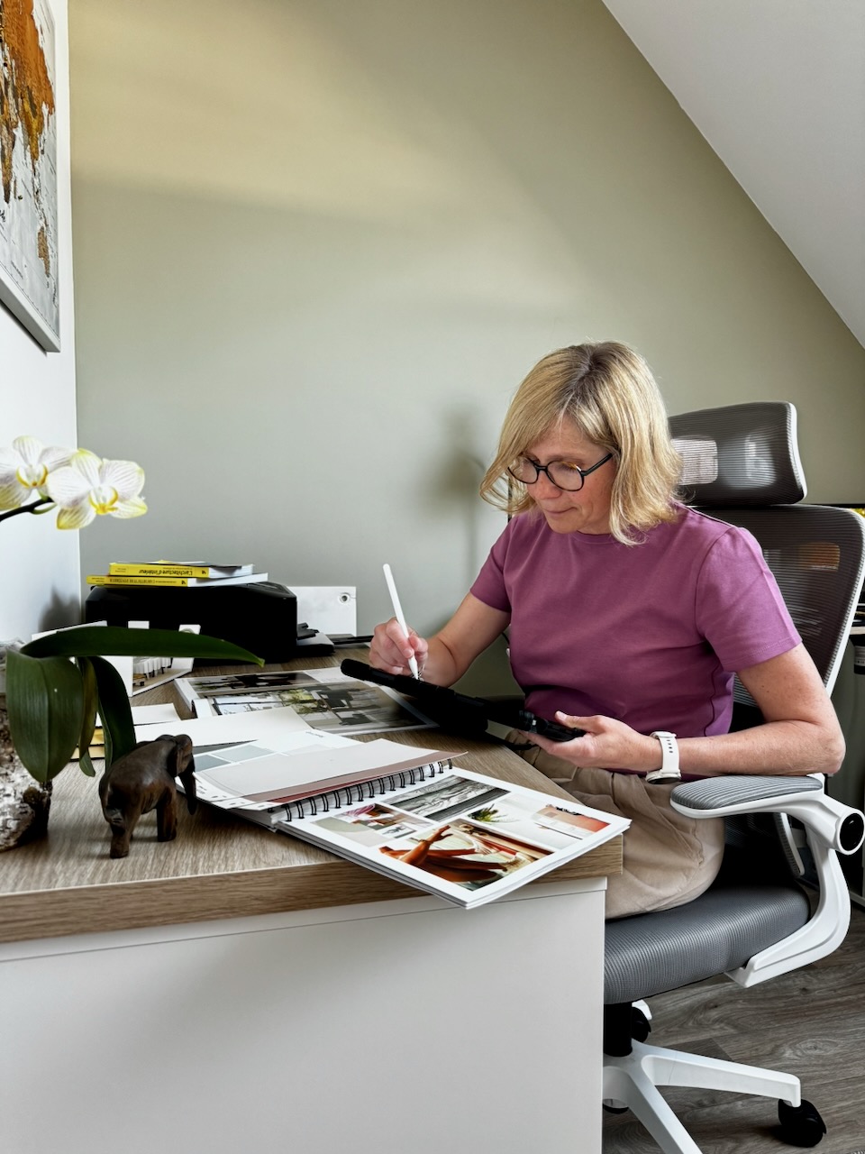 Femme travaillant à un bureau avec des échantillons et des livres de design, prenant des notes avec une tablette.